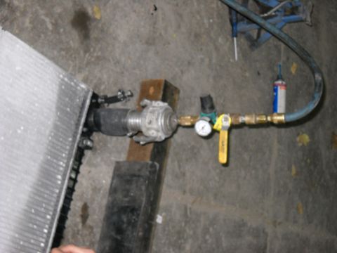 1986 Ford C-350 (Centurion Conversions) - Radiator pressure testing equipment connected to a radiator, a gauge and a yellow handle valve for repair.