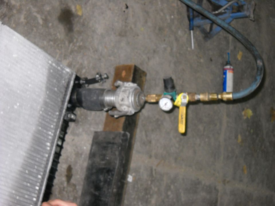 Radiator on a shop floor rigged to a brass valve, gauge and air hose for a pressure test