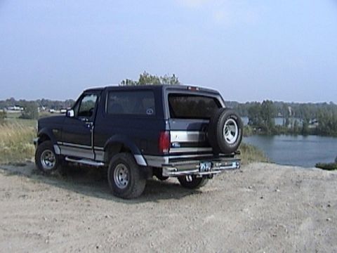 1995 Ford Bronco - A dark blue Ford Bronco is parked on a dirt path overlooking a body of water.