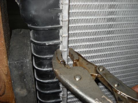 1986 Ford C-350 (Centurion Conversions) - Pliers are used to grip the side of a vehicle radiator during a repair process.