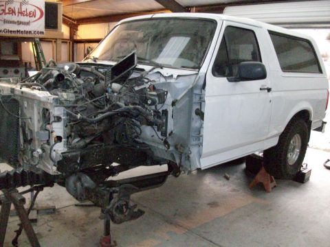 1996 Ford Bronco - White Ford Bronco undergoing front-end repair, engine compartment visible.