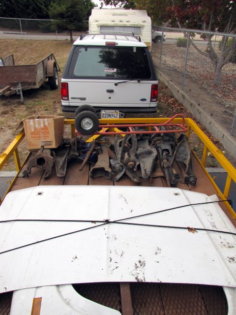 1984 Ford Bronco - A white Ford Explorer is parked behind a trailer carrying various car suspension parts and a hood.