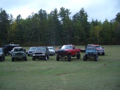 1994 Ford F-250 - Several lifted trucks and SUVs are parked on a grassy field with a forest in the background.