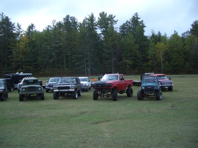 1994 Ford F-250 and other lifted trucks and SUVs parked on grass with trees in background