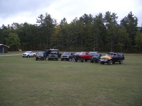 1994 Ford F-250 - A collection of modified trucks and SUVs are gathered together in an open field under a cloudy sky.
