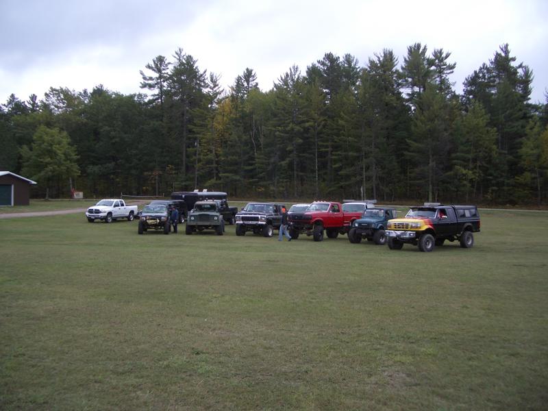 Several trucks and SUVs parked on a grassy field with trees in the background