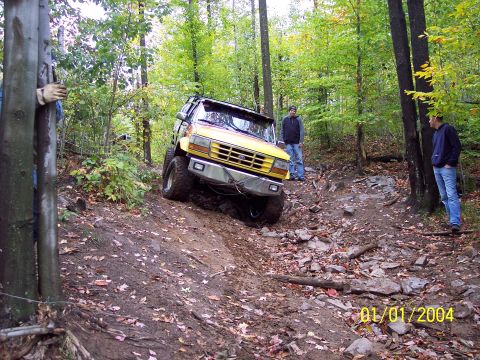 1994 Ford F-250 - Yellow truck navigates a challenging off-road course in a wooded area. The date 01/01/2004 is visible.