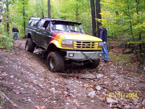 1994 Ford F-250 - Off-road pickup truck with a camper shell navigates a rocky, wooded trail.