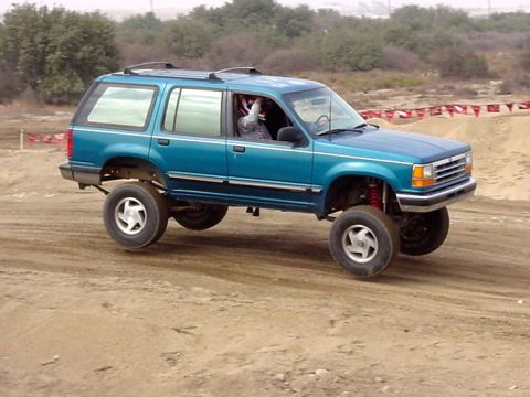 1984 Ford Bronco - This lifted Ford Explorer is navigating a dirt track, with the driver sporting a helmet.