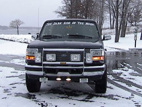 1995 Ford Bronco - A Ford truck is parked in a snowy landscape, a prominent grille guard and custom text on its windshield.
