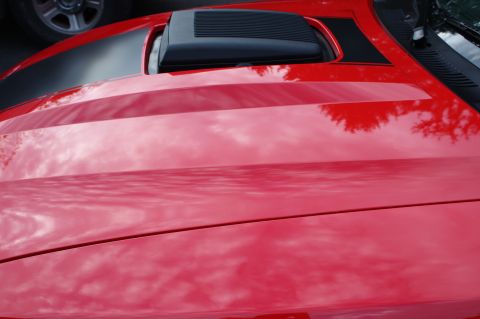 2004 Ford Mustang - A red car hood with black racing stripes and a hood scoop shows reflections of the sky and trees.