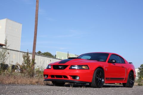 2004 Ford Mustang - A red 2004 Ford Mustang coupe is shown from a three-quarter front view, black racing stripes on the hood and sides.