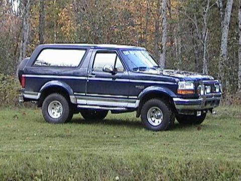 1995 Ford Bronco - This 1995 Ford Bronco is seen from a three-quarter front view, parked outdoors on a grassy area with trees.