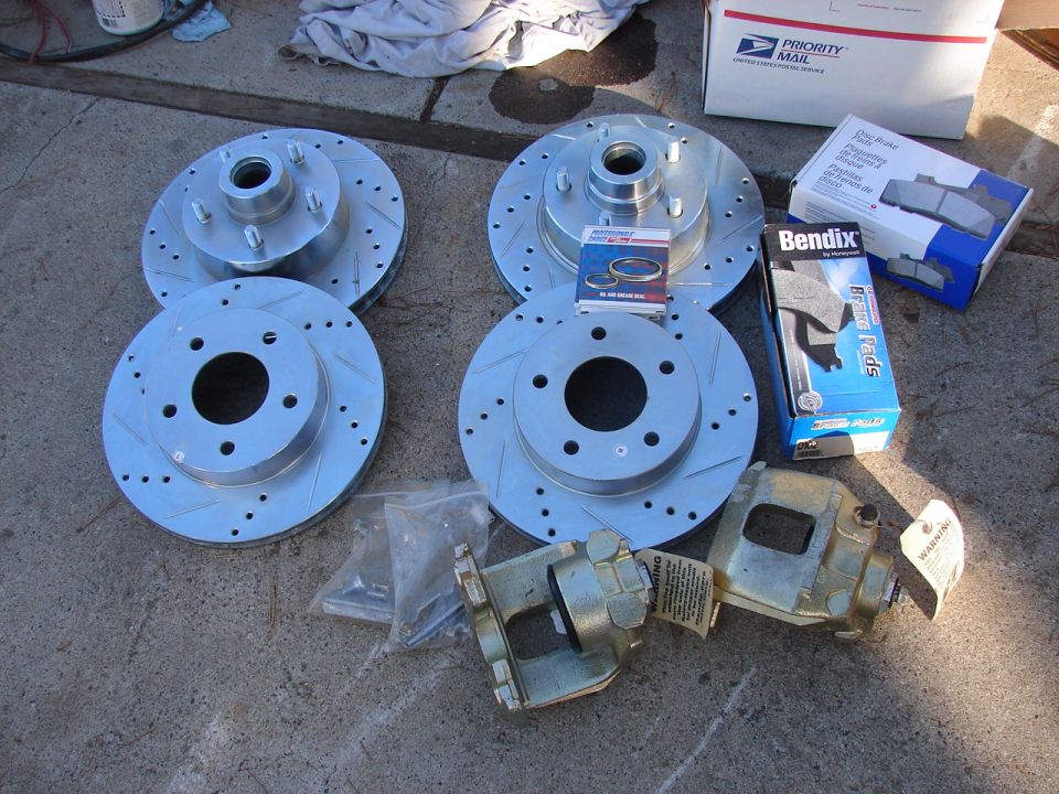 Four slotted brake rotors and two brake calipers with boxes of Bendix brake pads