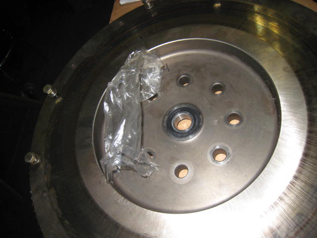 Round metal flywheel with center hub and bolt holes on a workbench