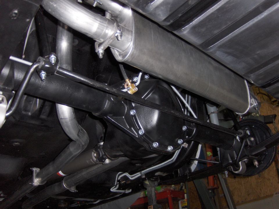 Underside view of a car's rear axle, differential, and exhaust system. Shows leaf springs and brake drums