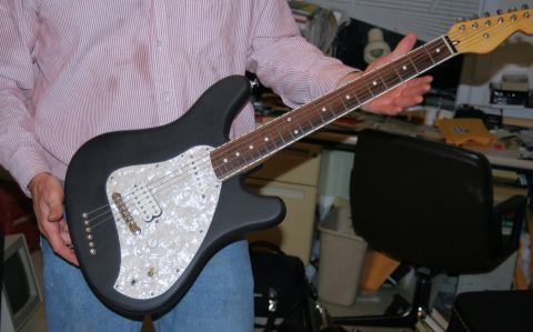 1976 Ford Ranchero - A person is holding a black electric guitar with a white pearloid pickguard and a maple fretboard.