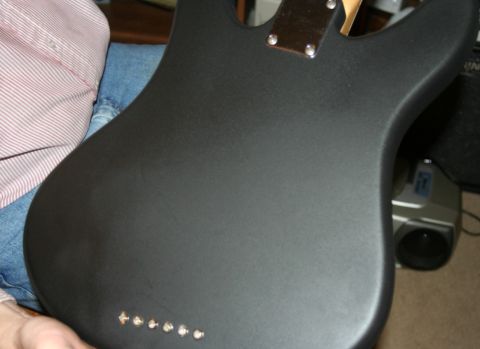 1976 Ford Ranchero - The back of a black electric guitar body is shown, with visible hardware and a person in casual clothing.