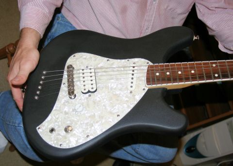 1976 Ford Ranchero - A person holds a black electric guitar a white pearloid pickguard and dual humbucker pickups.
