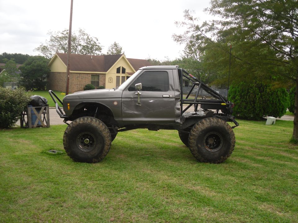 Gray modified pickup truck with large tires and roll cage, parked on a lawn