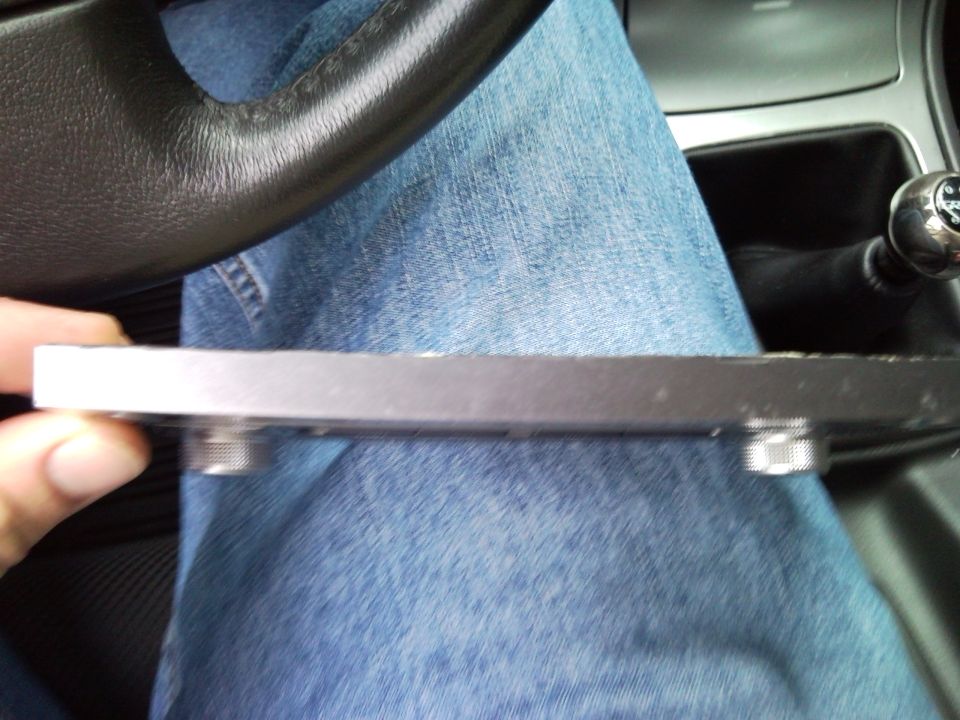 Metal plate with screws held in front of denim jeans, with a car steering wheel and gear shift visible