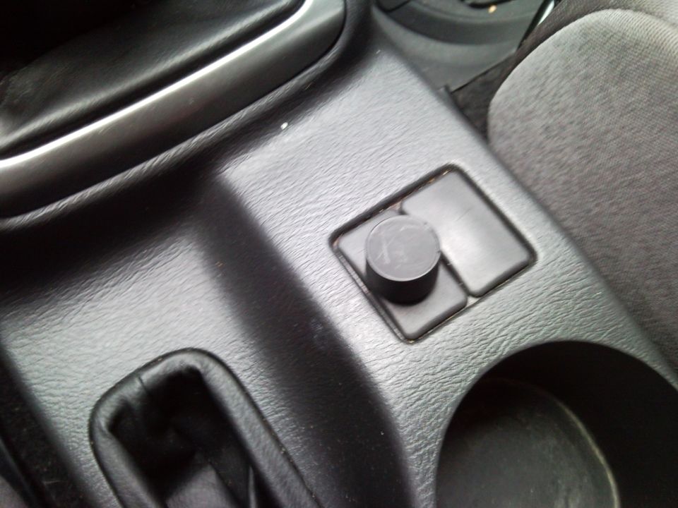 Center console with a black circular knob and two rectangular buttons, next to a cup holder
