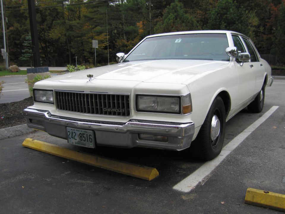 White Chevrolet Caprice sedan parked, front view. Chrome grille, rectangular headlights, license plate 242 8516