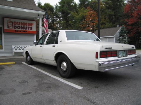 1991 Ford LTD Crown Victoria - A white Chevrolet Caprice sedan is parked in a lot next to a Dunkin' Donuts with fall foliage in the background.