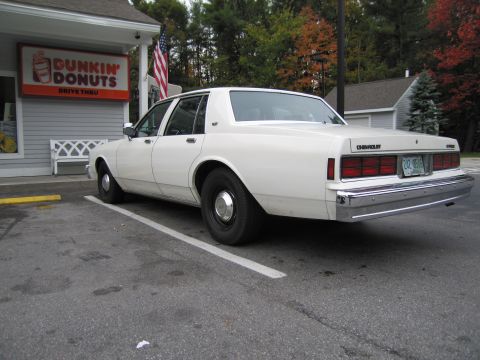 1991 Ford LTD Crown Victoria - A white sedan is parked in front of a Dunkin' Donuts, showing its rear profile.