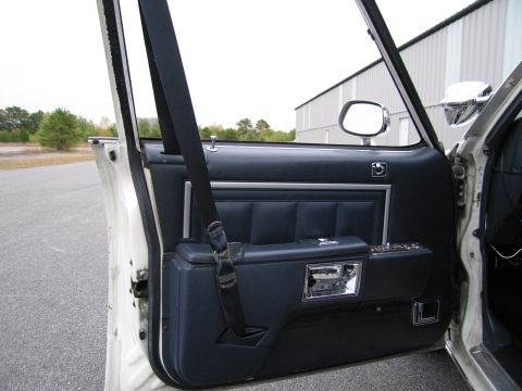 1991 Ford LTD Crown Victoria - The interior door panel of a car shows dark blue upholstery and a chrome door handle.