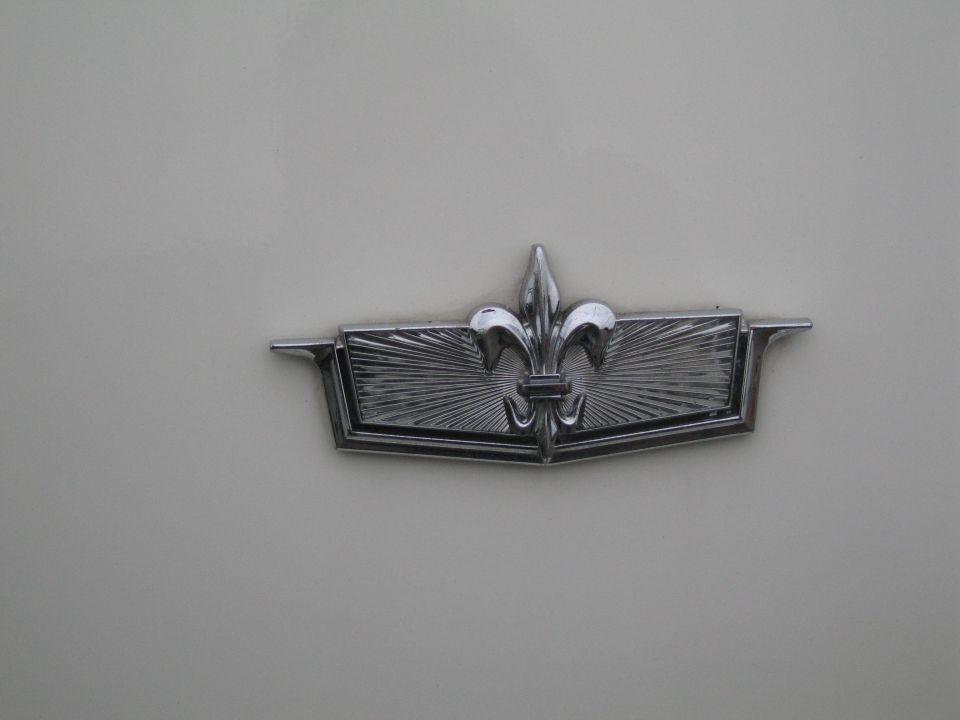 close-up of a chrome emblem with a fleur-de-lis on a cream-colored car