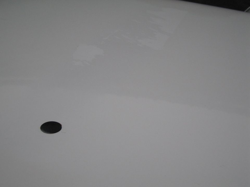 White car panel with a black circular object, possibly a sensor or emblem mount