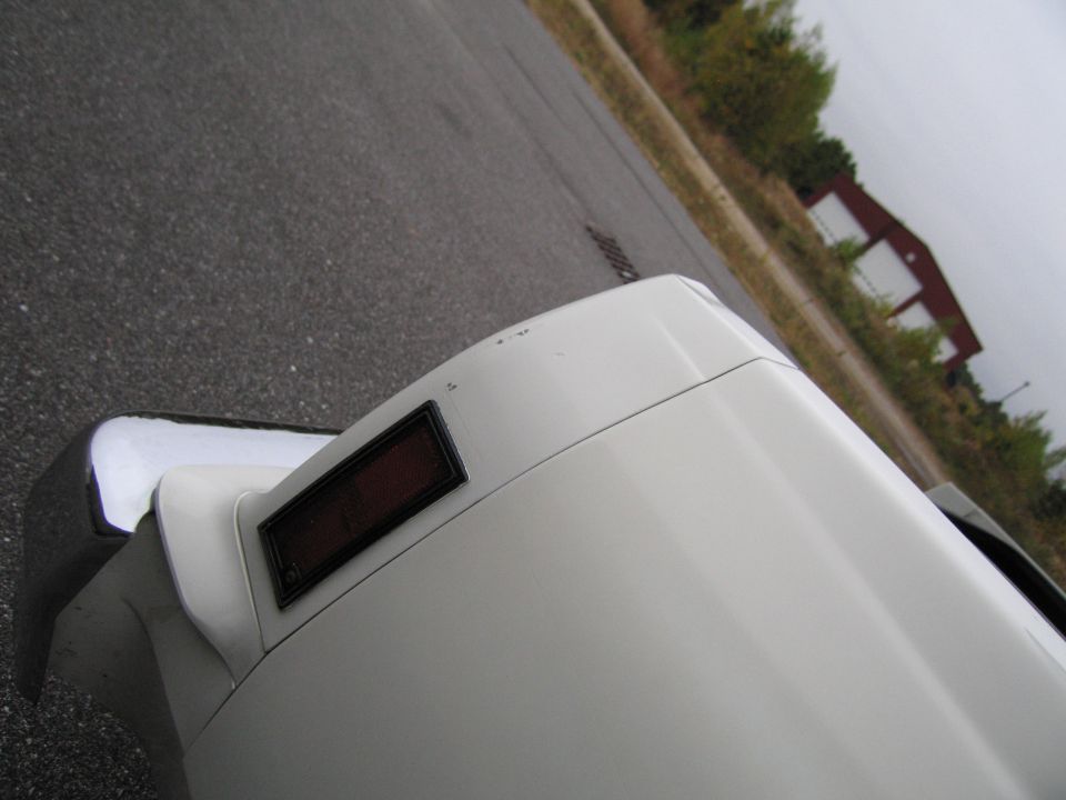 White car's rear corner with chrome bumper and red reflector