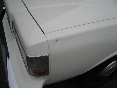 1991 Ford LTD Crown Victoria - Close-up of a white car's rear quarter panel, showing a dent and a damaged taillight assembly.