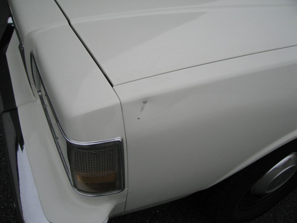 White car rear quarter panel with a dent and a damaged taillight