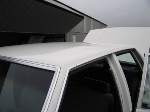1991 Ford LTD Crown Victoria - Close-up view of a white sedan's roofline and interior, with the hood open.