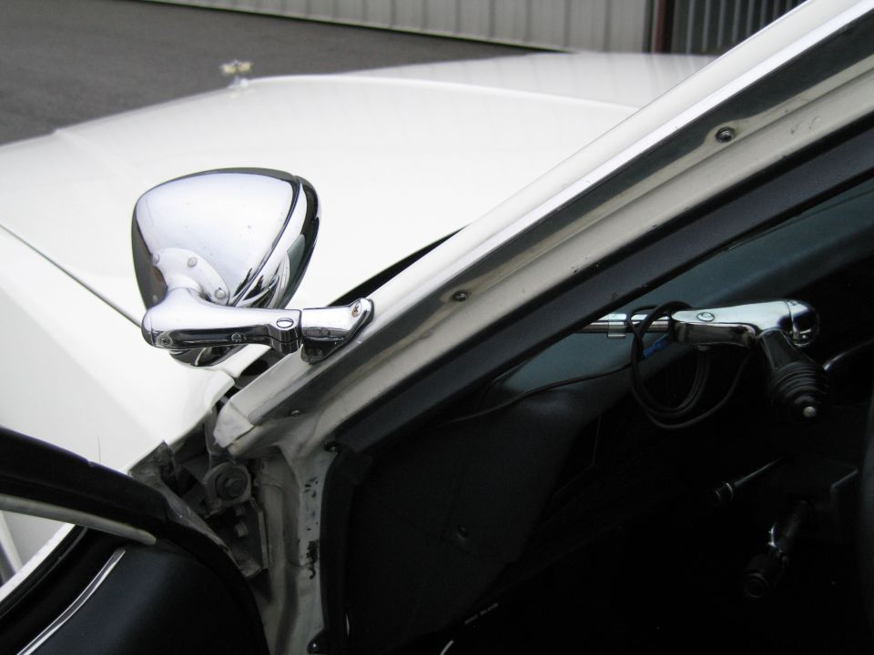 Chrome side mirror on a white car. Interior shows steering column and part of the dashboard