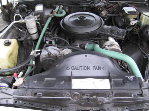 1991 Ford LTD Crown Victoria - The engine bay of a vehicle, a prominent fan shroud with a "CAUTION FAN" warning and green hoses.