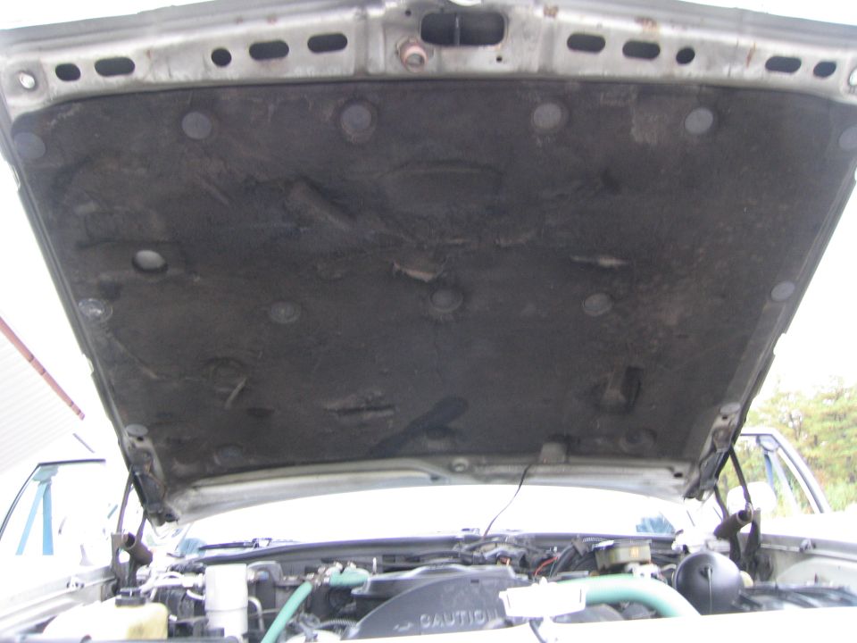 Under hood insulation and engine bay of a car. Fan shroud has 'CAUTION' text