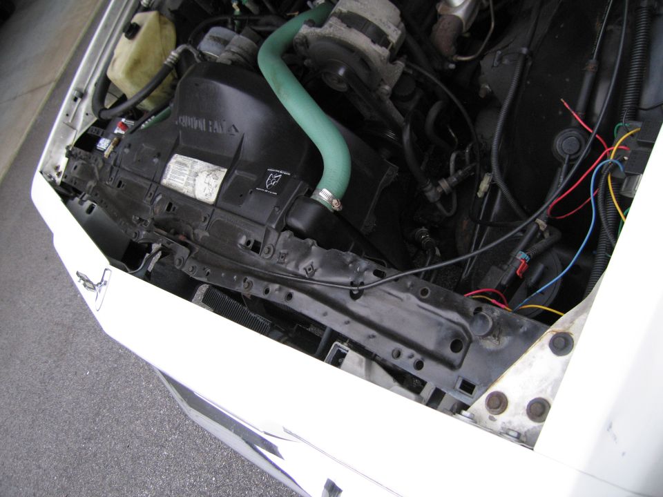 Close-up of a car's engine bay, showing the radiator fan, hoses, and wiring