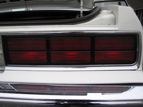 1991 Ford LTD Crown Victoria - The rear of a white car displays its triple rectangular taillights and chrome bumper, with the trunk open.