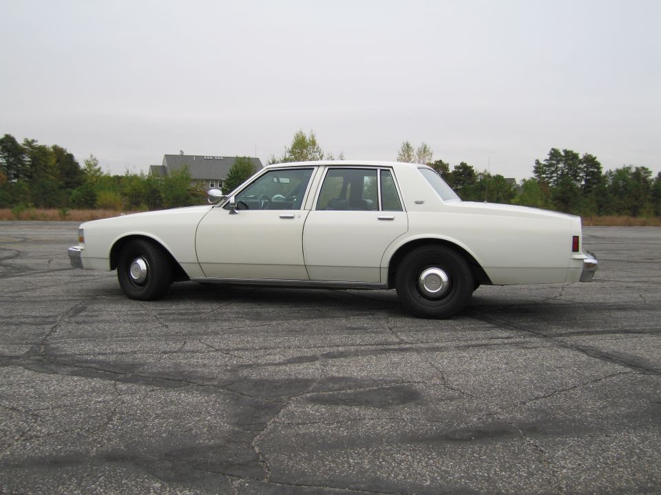 White 1990 Chevrolet Caprice sedan, side view, parked on cracked asphalt