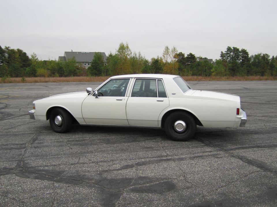 White sedan side view. Appears to be a 1990 Chevrolet Caprice