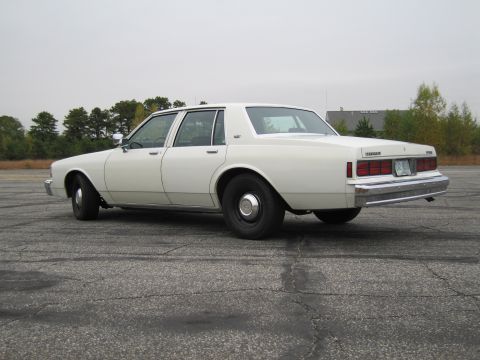1991 Ford LTD Crown Victoria - Rear view of a white sedan, possibly a 1980s Chevrolet Caprice, on an asphalt lot.
