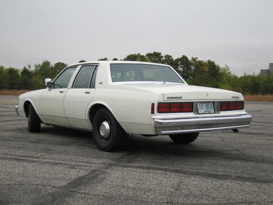 White Chevrolet Caprice sedan from rear 3/4 angle, showing chrome bumper, rectangular taillights, and license plate 242-8516