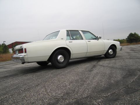 1991 Ford LTD Crown Victoria - Side view of a white sedan, possibly a Chevrolet Caprice from the 1980s, on an overcast day.