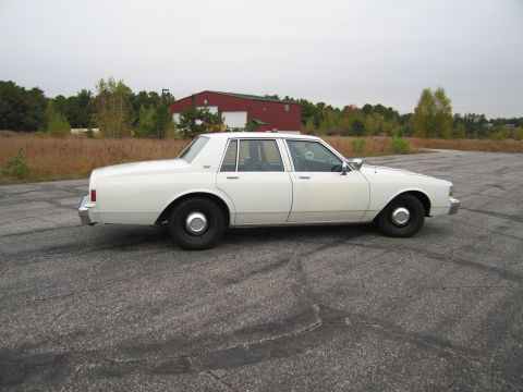 1991 Ford LTD Crown Victoria - A white sedan is parked on an asphalt lot with a red building in the background.