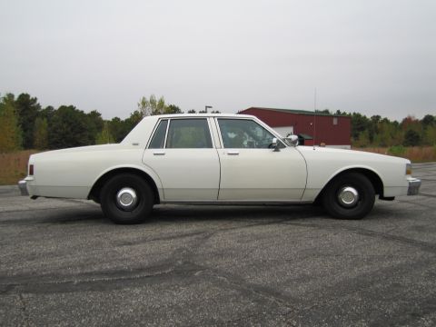 1991 Ford LTD Crown Victoria - White 1990 Chevrolet Caprice sedan parked on asphalt with a red building in the background.