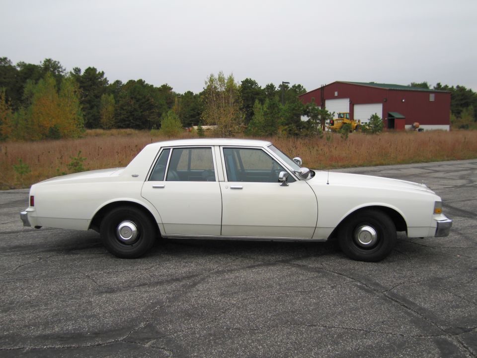 White sedan parked on asphalt with a red building in the background