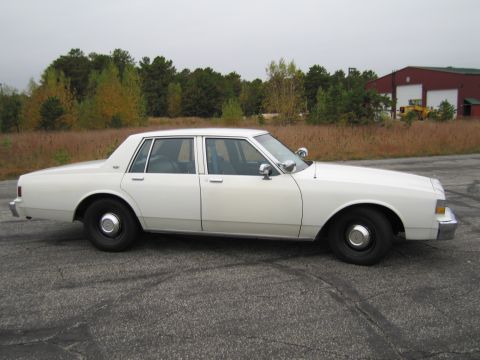 1991 Ford LTD Crown Victoria - This white sedan, likely a former police or taxi vehicle, is shown from the side. The body style suggests a 1991 model year.